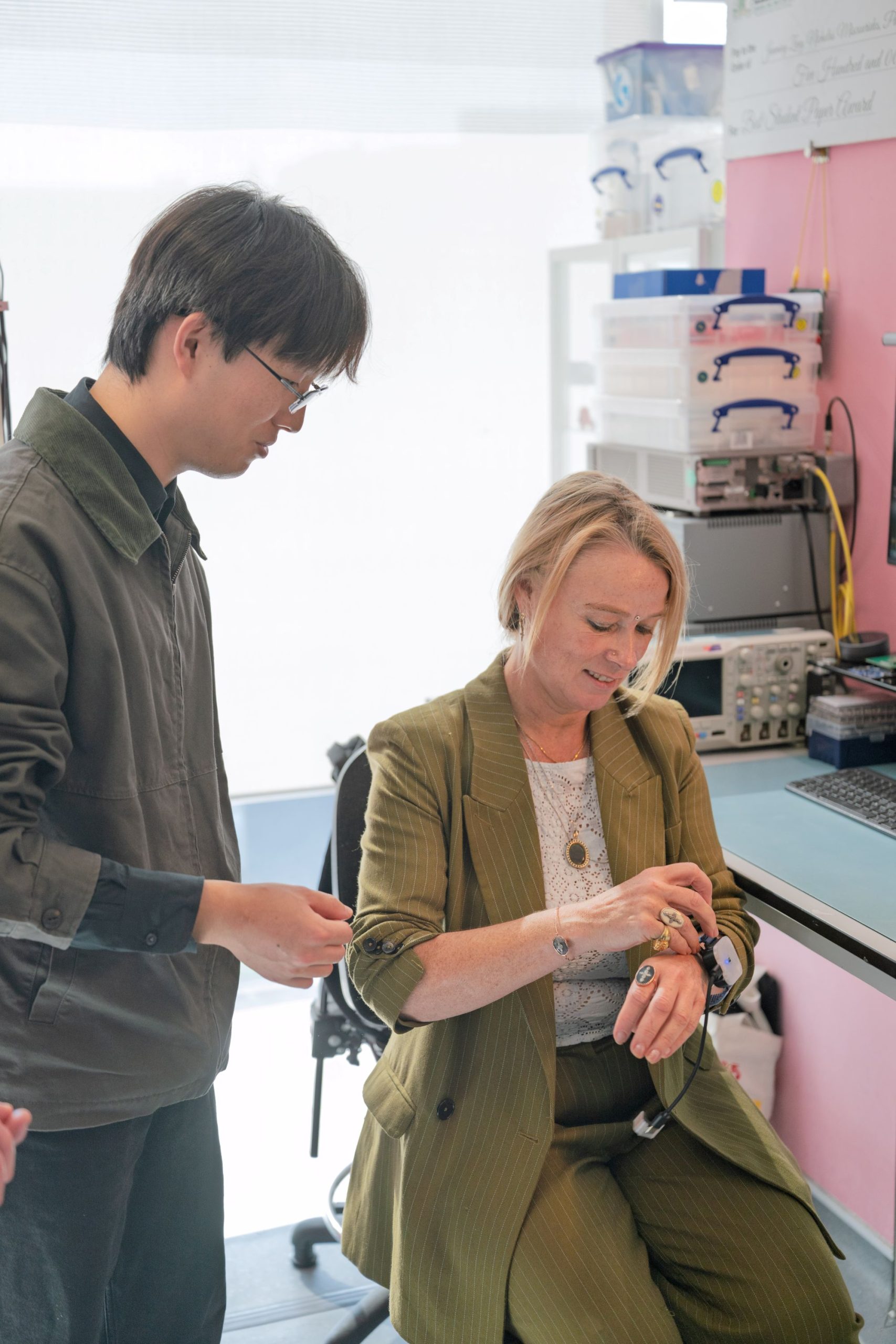 A woman sitting, tries on the D-SCAPE prototpye while a researcher watches